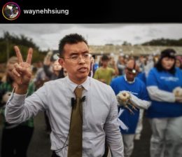 Wayne holds up his right hand making a “peace” sign, as he walks along with 600 animal advocates while they openly rescue dying chickens from factory farming conditions